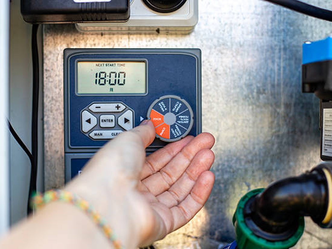 A Grolife crew member checking and adjusting an irrigation controller on a commercial site