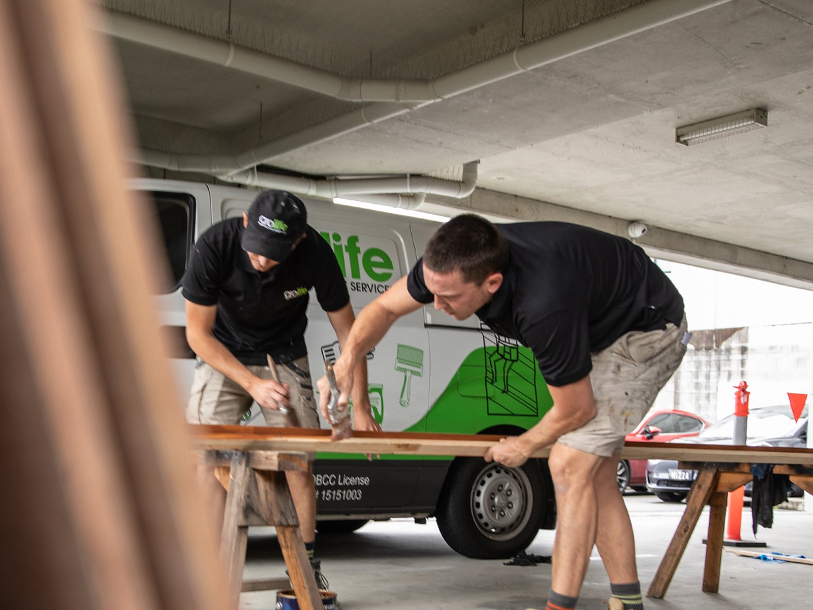 Grolife Property Services crew painting timber lengths beside a branded service van